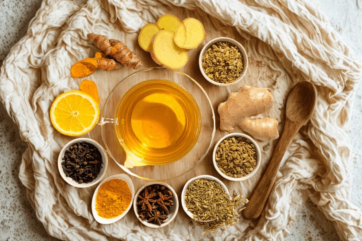 Flat lay of ginger root, turmeric, fennel, and a steaming cup of golden herbal tea arranged on linen, representing natural digestion remedies and Ayurvedic gut healing.