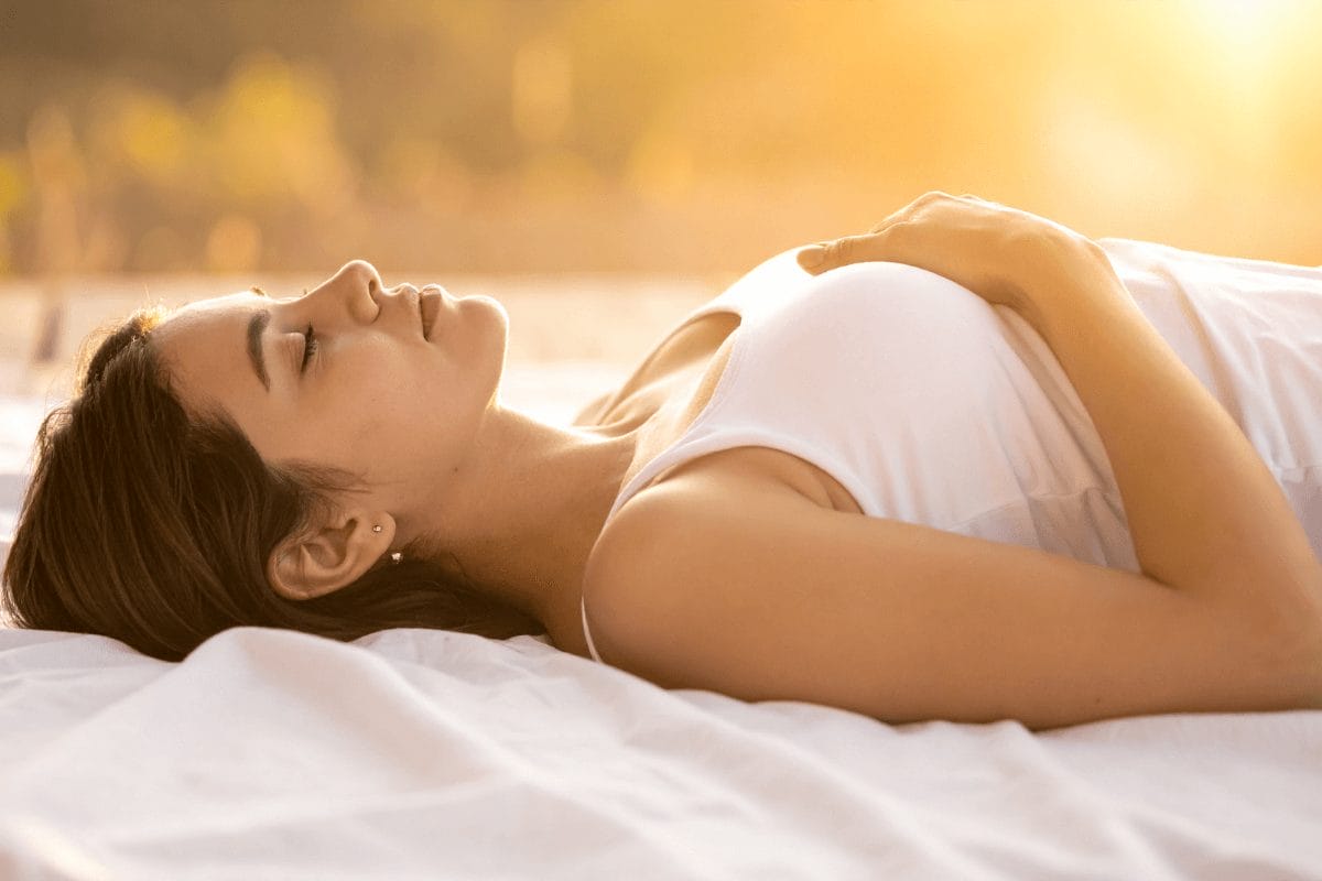 A woman resting peacefully on a white bed bathed in warm golden light, symbolizing emotional balance, rest, and mindful surrender. The calm tones evoke release and inner softness.